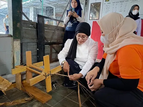 Perempuan perajin menganyam serat alam dengan alat kayu, ditemani rekan di sebelahnya