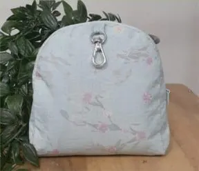 Tas kain biru muda berbentuk kubah bermotif bunga merah muda dengan kait logam, di atas meja kayu