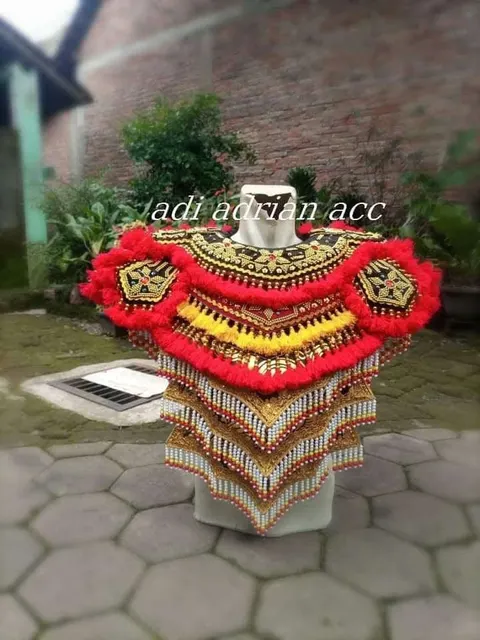 Hiasan bahu dan dada kostum tari berwarna merah, emas dan kuning dengan rumbai manik pada manekin di halaman