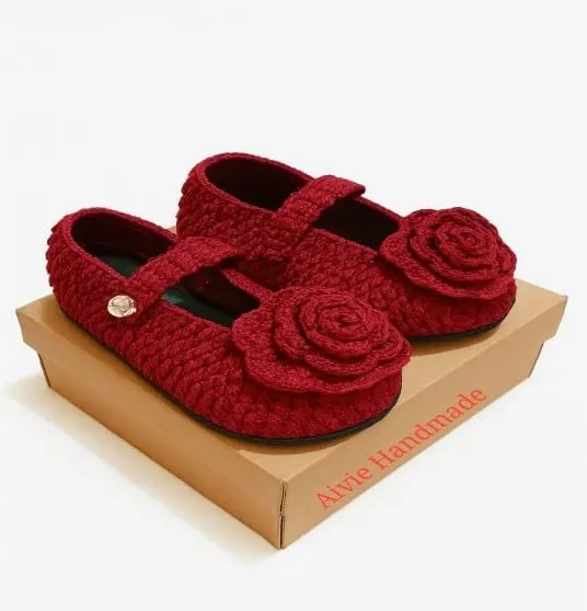 Sepasang sepatu rajut merah berhias bunga mawar rajut di atas kotak kraft bertulisan Aivie Handmade