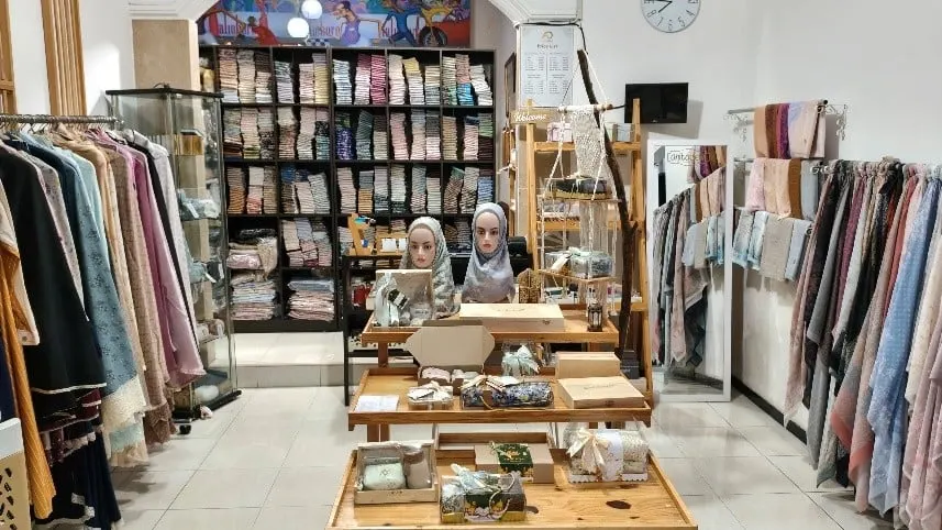 Ruang toko dengan rak hijab terlipat, dua kepala manekin berhijab dan meja kayu berisi kotak hampers