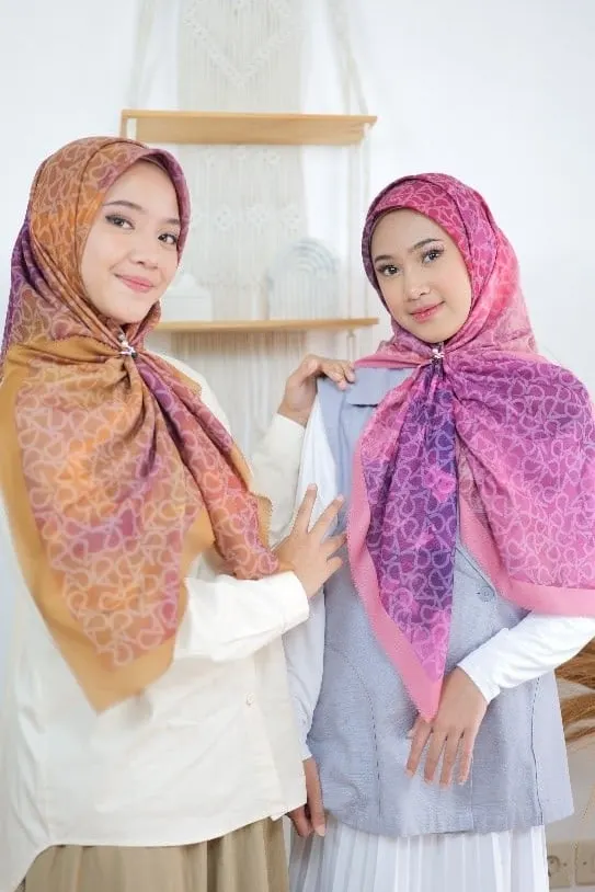 Dua model memakai hijab segi empat motif oranye dan ungu merah muda bersemat bros, foto dalam posisi miring