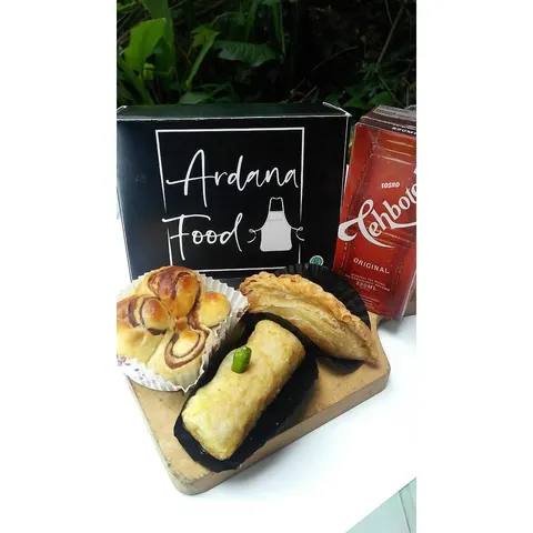 Roti, pastry, dan gorengan dengan cabai rawit di talenan kayu, di depan kotak hitam Ardana Food dan teh kotak