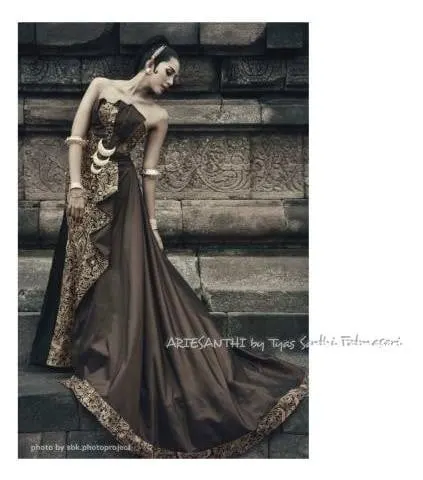 Model memakai gaun kemben cokelat berekor panjang dengan aksen batik di depan dinding candi