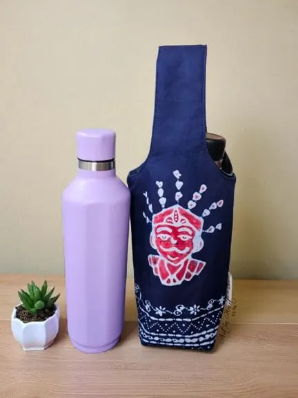 Tas botol minum batik biru tua bermotif ondel-ondel merah di samping botol minum ungu dan pot kaktus