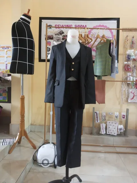 Manekin memakai setelan blazer, rompi dan celana hitam di ruang jahit dengan rak vest dan aksesori