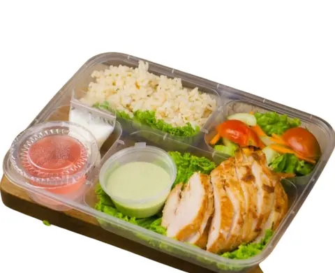 Kotak makan bersekat berisi nasi merah, ayam panggang iris, salad sayur dan dua cup saus