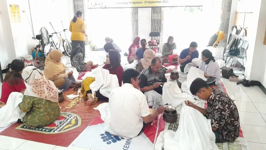 Peserta pelatihan duduk di lantai sambil membatik kain putih dengan canting dan wajan malam