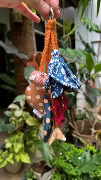 Gantungan kunci dari kain perca batik dengan tali kepang oranye, digantung di depan tanaman