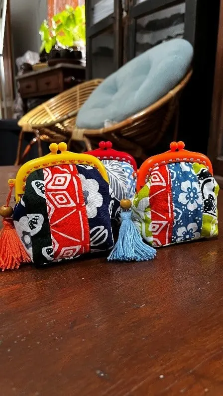 Tiga dompet koin perca batik merah dan biru berbingkai logam dengan rumbai, di atas meja kayu