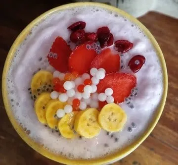 Smoothie merah muda dalam mangkuk kuning dengan potongan pisang, stroberi, ceri dan mutiara sagu