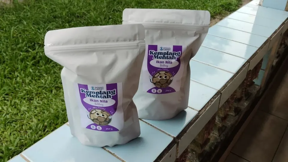Dua kemasan pouch putih Kemplang Mentah Ikan Nila 250 g berlabel ungu di atas bangku keramik dekat rumput
