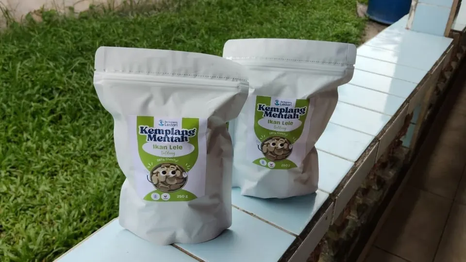 Dua kemasan pouch putih Kemplang Mentah Ikan Lele 250 g berlabel hijau di atas bangku keramik dekat rumput