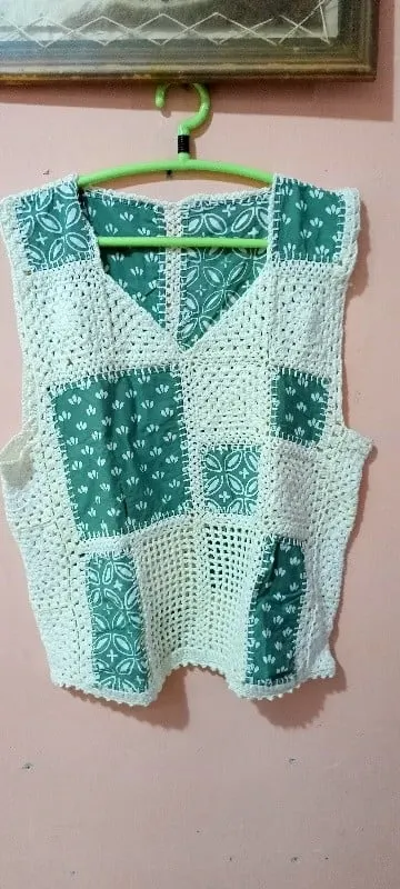 Vest rajut putih dengan tambalan kain motif hijau tergantung pada hanger di dinding merah muda