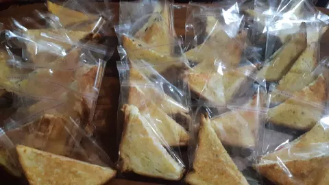 Potongan roti bakar berbentuk segitiga dalam kantong plastik bening tersusun di atas meja
