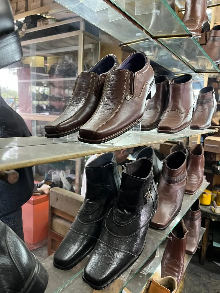 Rak kaca toko berisi deretan sepatu kulit pria warna cokelat dan hitam