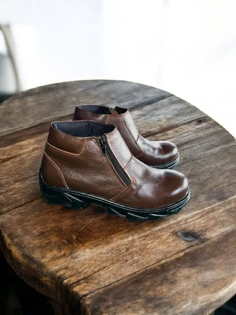 Sepasang sepatu boots pendek kulit cokelat dengan resleting samping di atas meja kayu bundar