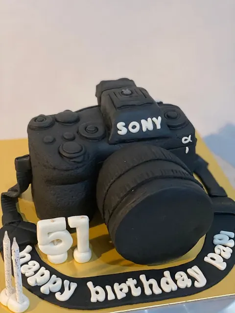 Kue ulang tahun berbentuk kamera hitam bertulisan Sony dengan angka 51 dan tulisan happy birthday