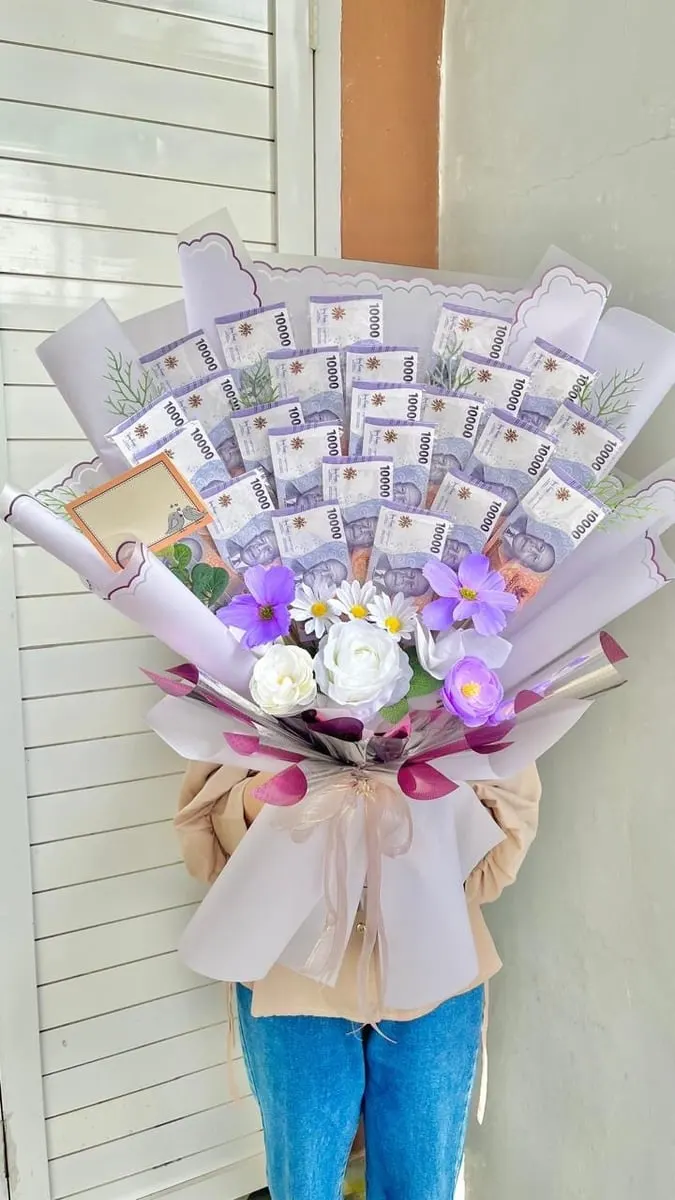 Buket besar berisi lembaran uang sepuluh ribu rupiah, bunga putih dan ungu, dibungkus kertas warna lilac