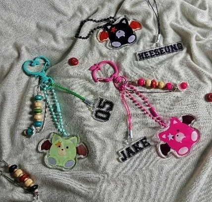 Tiga gantungan kunci warna-warni dengan manik-manik, figur kucing akrilik dan label nama di atas kain krem