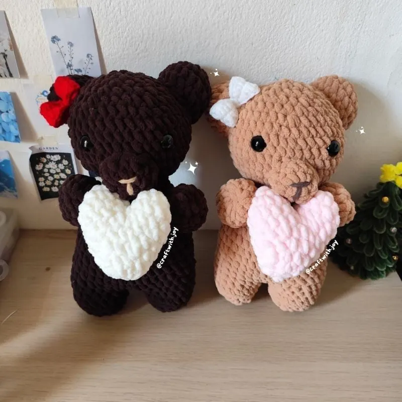 Dua boneka rajut beruang cokelat tua dan cokelat muda memeluk hati putih dan merah muda di atas meja