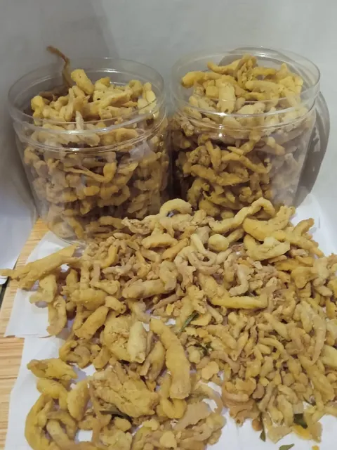 Dua toples dan tumpukan keripik jamur goreng berwarna kuning kecokelatan di atas kertas