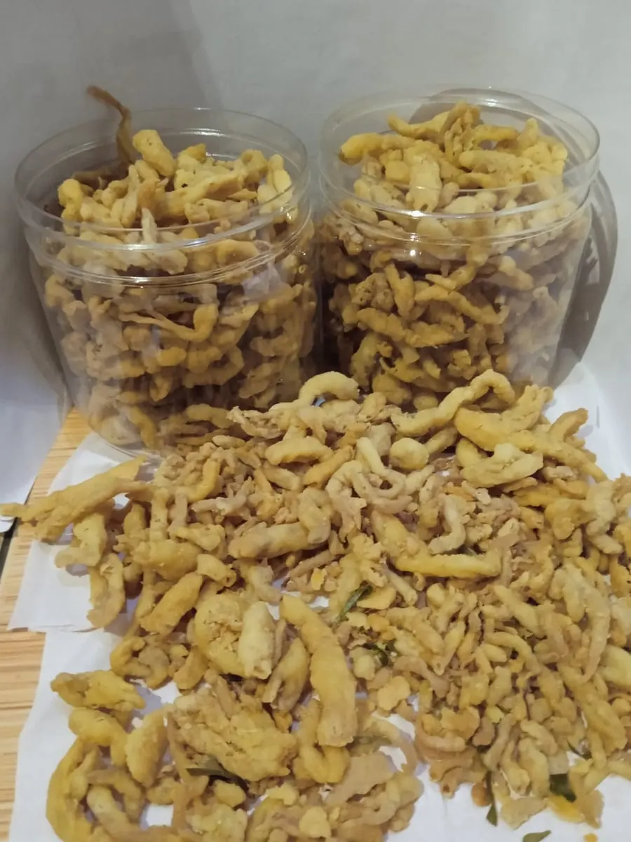 Dua toples dan tumpukan keripik jamur goreng berwarna kuning kecokelatan di atas kertas