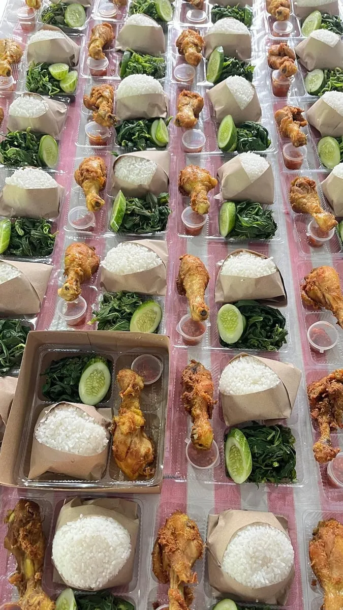 Puluhan nasi kotak berisi nasi bungkus, ayam goreng, sayur hijau, jeruk nipis dan sambal tersusun di meja