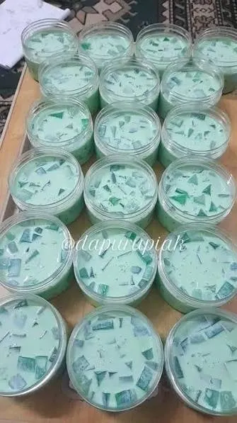 Deretan puding hijau dengan potongan jeli dalam cup plastik bening di atas meja kayu