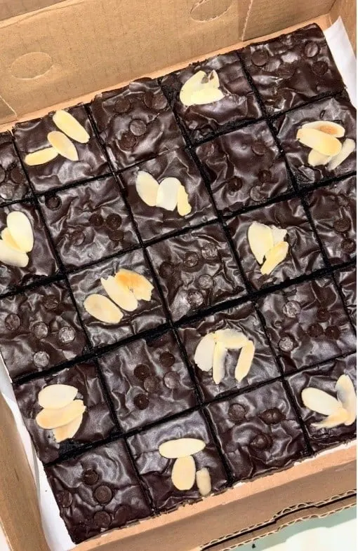Brownies cokelat dalam kotak karton, dipotong persegi dengan chocochip dan irisan almon di atasnya