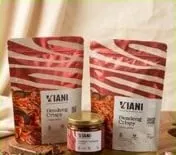 Dua kemasan standing pouch VIANI Dendeng Crispy dan satu botol kaca kecil di atas papan kayu
