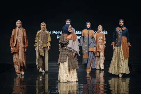 Enam model berhijab dan seorang perempuan berkacamata di runway mengenakan busana tenun cokelat, biru dan krem