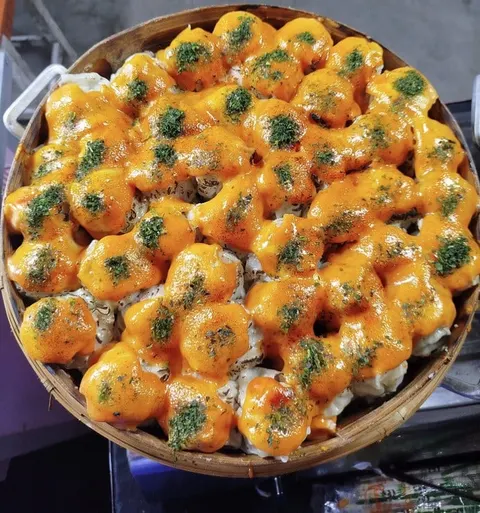 Dimsum bersaus mentai oranye dengan taburan nori hijau tersusun rapat dalam kukusan bambu