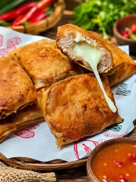 Dimsum goreng berkulit renyah terbelah memperlihatkan isian daging dan keju meleleh, dengan saus sambal