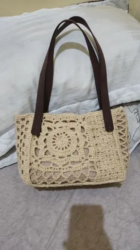Tas rajut krem bermotif bunga dengan tali cokelat tua di atas alas kain putih