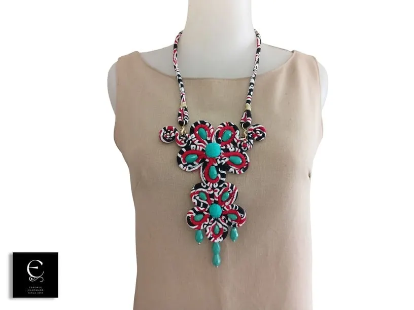 Kalung besar dari gulungan kain batik merah hitam dengan manik toska dipakai manekin bergaun krem