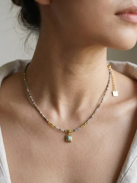 Leher perempuan memakai kalung manik kecil warna-warni dengan liontin batu hijau berbingkai emas