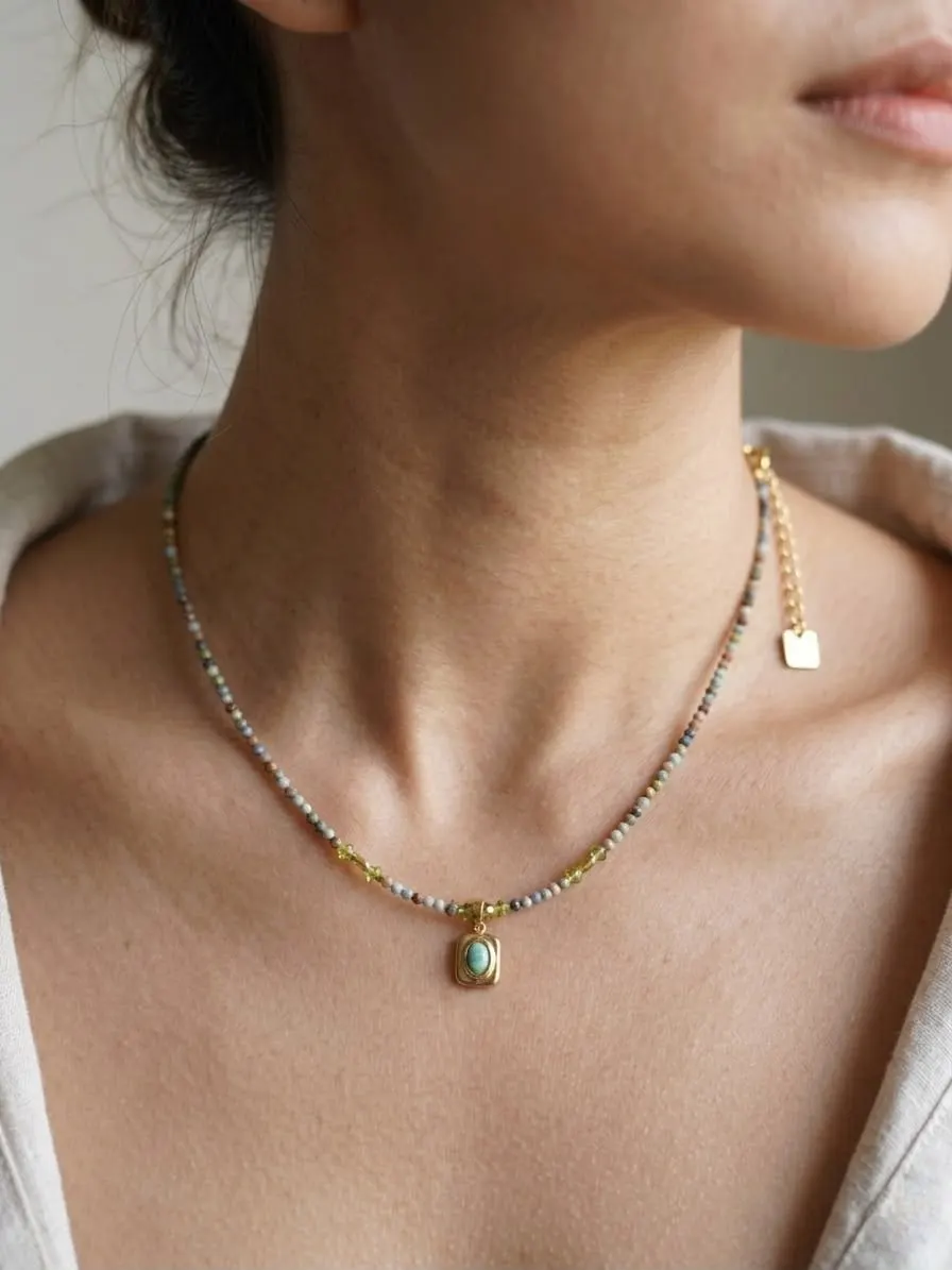 Leher perempuan memakai kalung manik kecil warna-warni dengan liontin batu hijau berbingkai emas