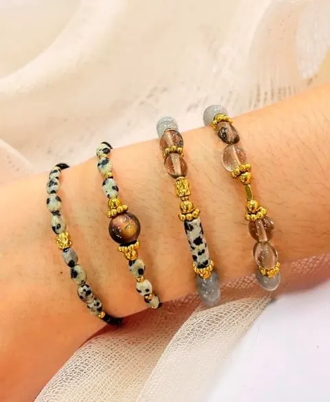 Empat gelang manik batu alam bertotol hitam putih dan cokelat bening dengan aksen emas di pergelangan tangan