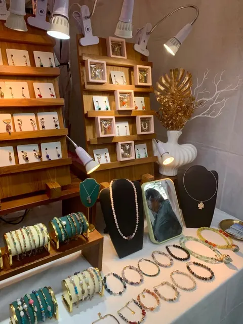 Meja pajang berisi deretan gelang manik, kalung di manekin leher dan anting pada kartu di rak kayu