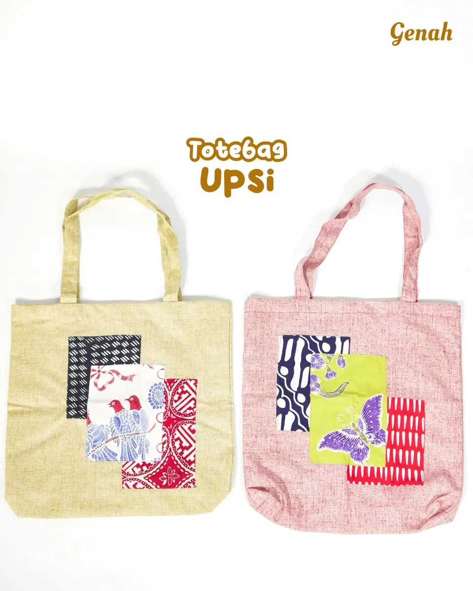 Dua tas jinjing kain krem dan merah muda dengan tempelan potongan kain motif, bertuliskan Totebag Upsi