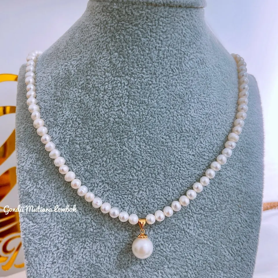 Kalung untaian mutiara putih dengan liontin satu mutiara pada manekin leher beludru abu-abu