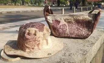 Topi bucket dan tas bermotif ecoprint daun merah keunguan di atas pagar beton di luar ruangan