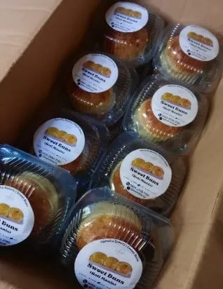Roti manis dalam wadah plastik bening berstiker Sweet Buns tersusun di dalam kardus