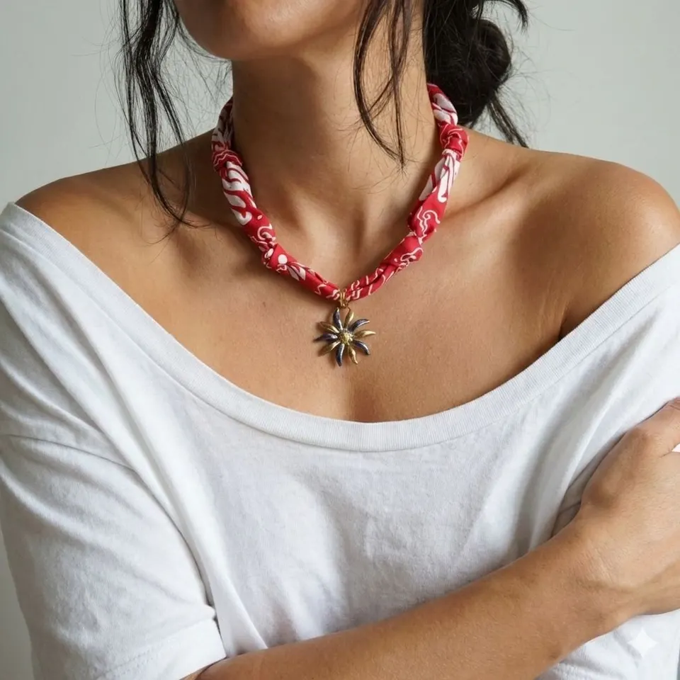 Perempuan berkaus putih memakai kalung dari lilitan kain merah bermotif putih dengan liontin bunga logam