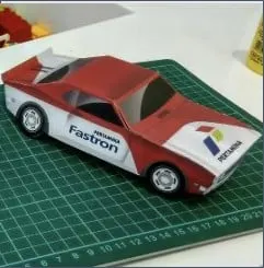 Papercraft mobil merah putih bercorak Pertamina Fastron di atas alas potong hijau