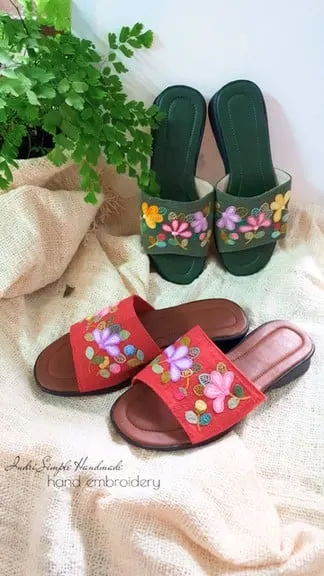 Sepasang sandal hijau dan sepasang sandal merah bersulam bunga warna-warni di atas kain krem