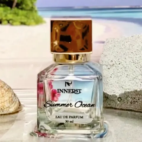 Botol parfum kaca kotak Innerst Summer Ocean 30 ml bertutup emas di antara kerang dan batu berlatar pantai