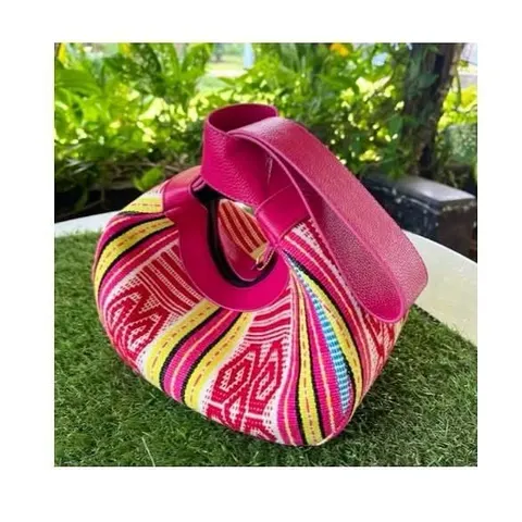 Tas tangan kulit merah muda berpadu kain tenun bergaris merah muda, kuning dan biru di atas rumput
