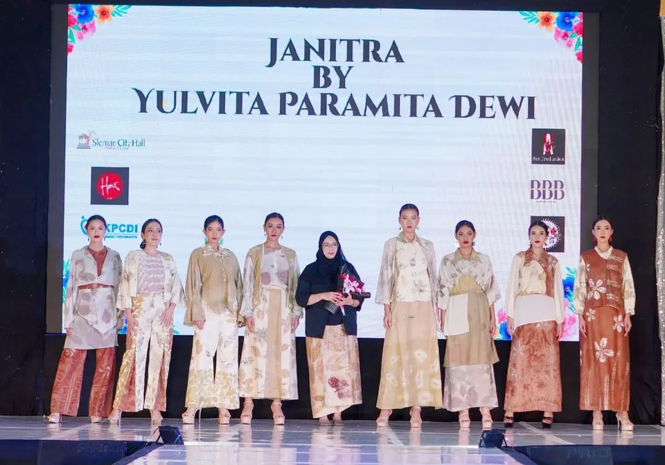 Delapan model di panggung peragaan busana mengenakan busana ecoprint krem dan cokelat di depan layar bertulisan Janitra